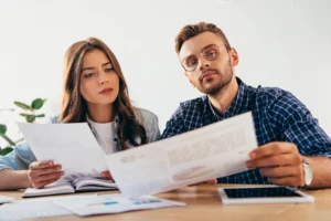 Hombre y mujer preocupados revisan documentos con gráficos y tablas en una mesa, reflejando el impacto de la bancarrota del Capítulo 13 en los co-firmantes.